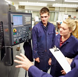 Students listening an experienced mechanic in front of a machine.